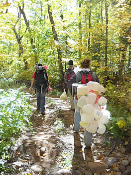 Group of people walking down a forest path carrying backpacks and plastic milk jugs