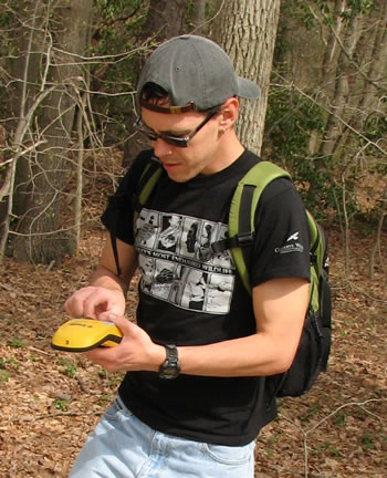 Man in woods wearing backpack holding gps units